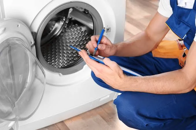 Repair specialist writing inspection notes beside a washing machine