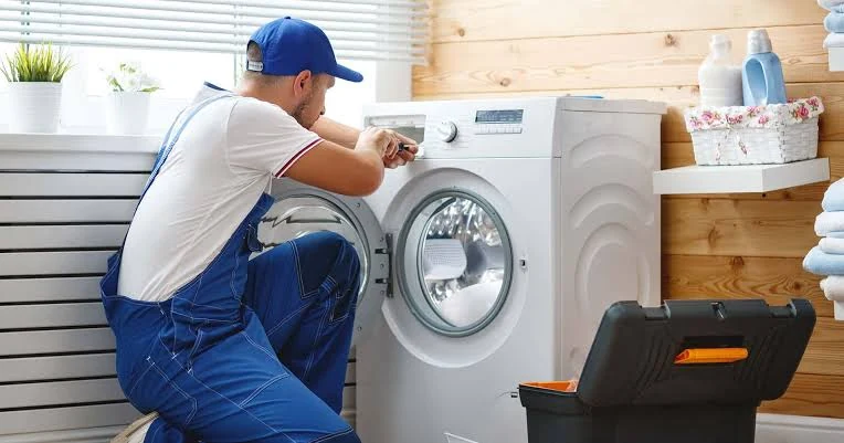 Repair specialist working on a front-loading washing machine in a home laundry room