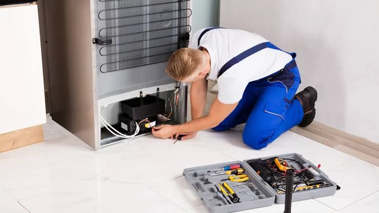 Technician inspecting the rear compressor of a refrigerator