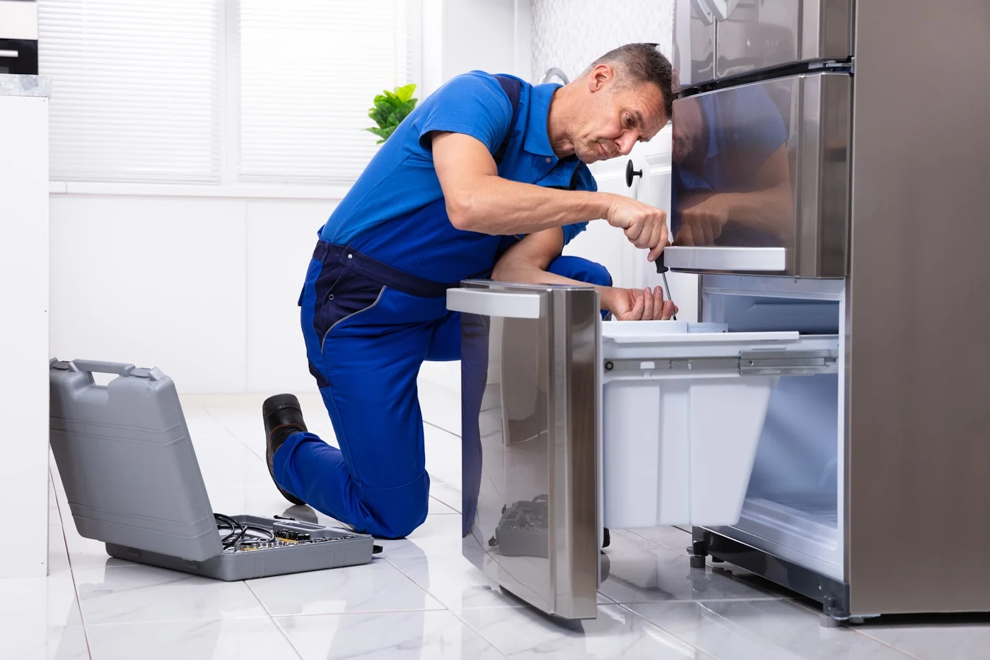 Appliance technician repairing the lower drawer of a stainless steel refrigerator